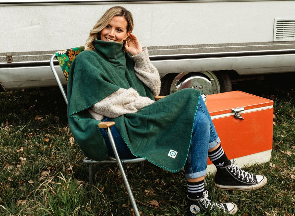 A lady sitting in a deck chair wearing a green camp blanket poncho
