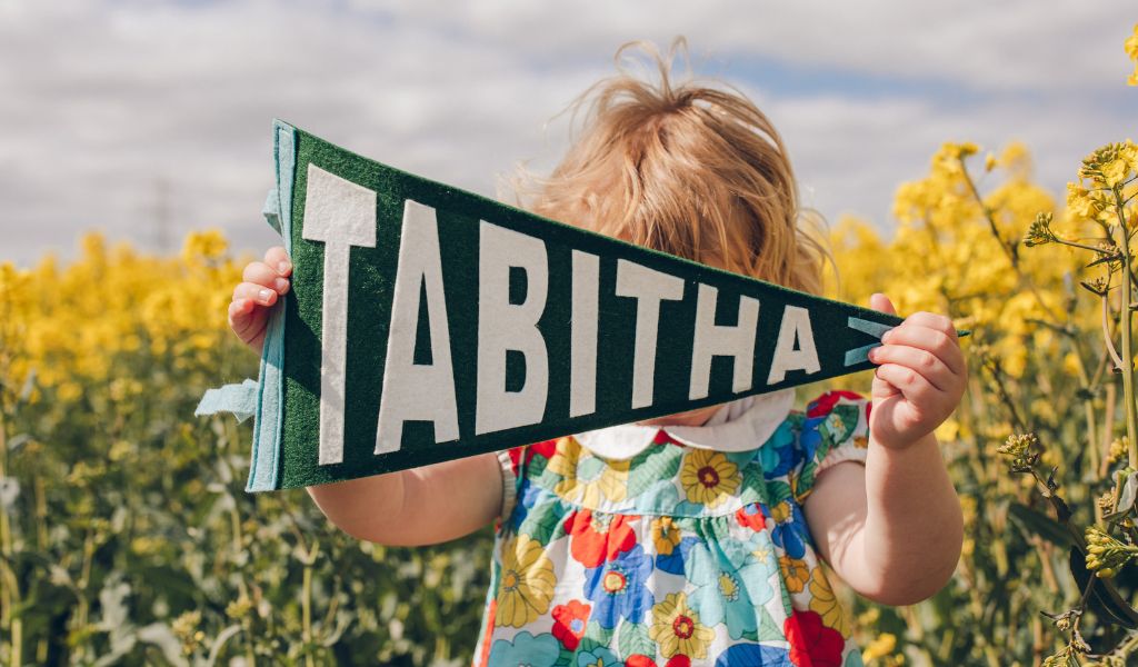 A girl in a field of flowers holding a personalised pennnat flag saying tabitha