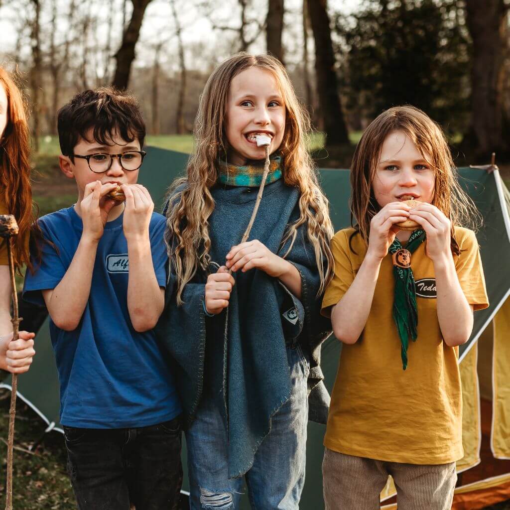 Three children eating marshmallows in front of a vintage tent