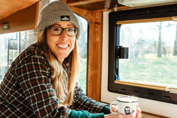 A lady in a beanie hat and check shirt leaning on a sideboard in a campervan