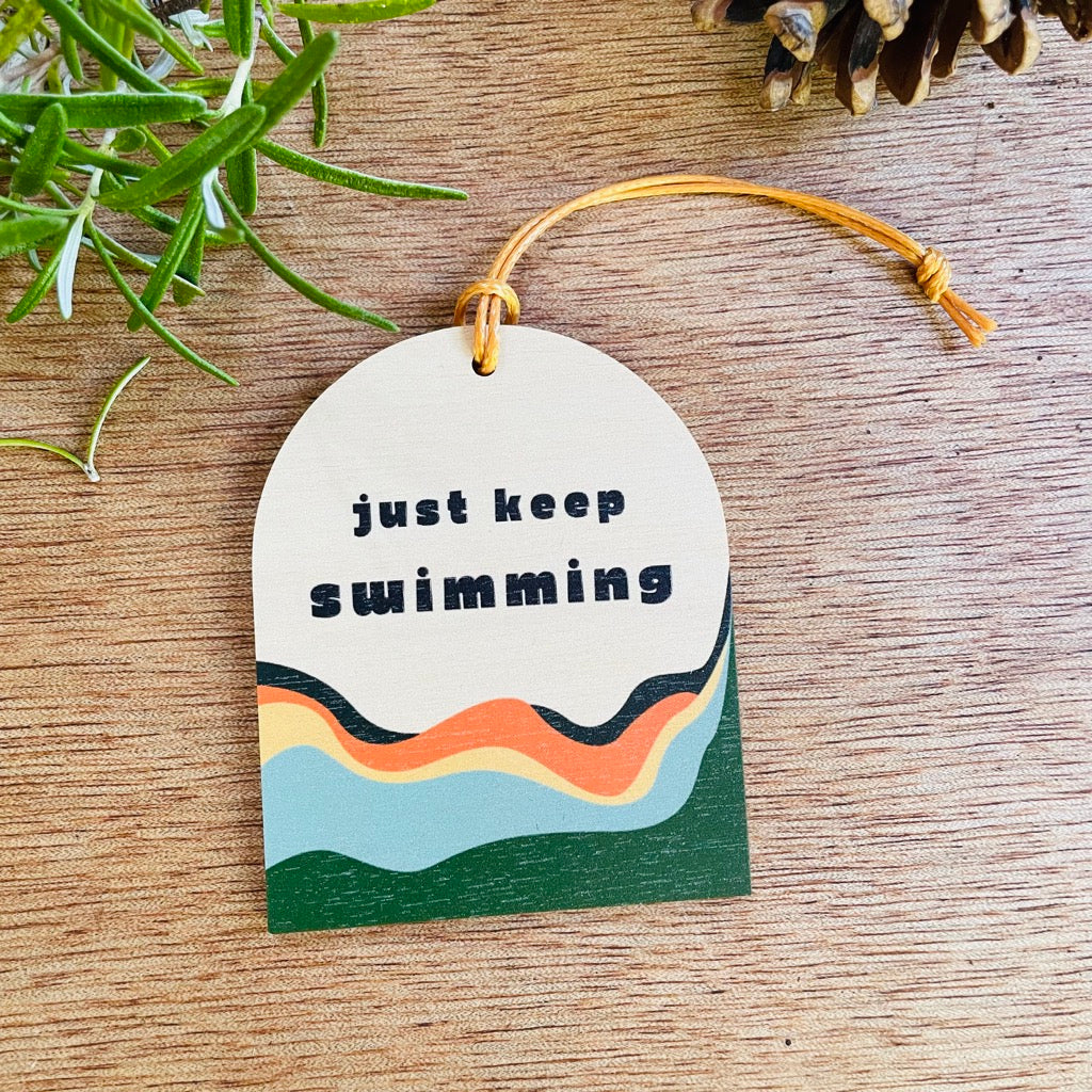 Wooden hanging decoration with the wording 'Just Keep Swimming' with colourful waves