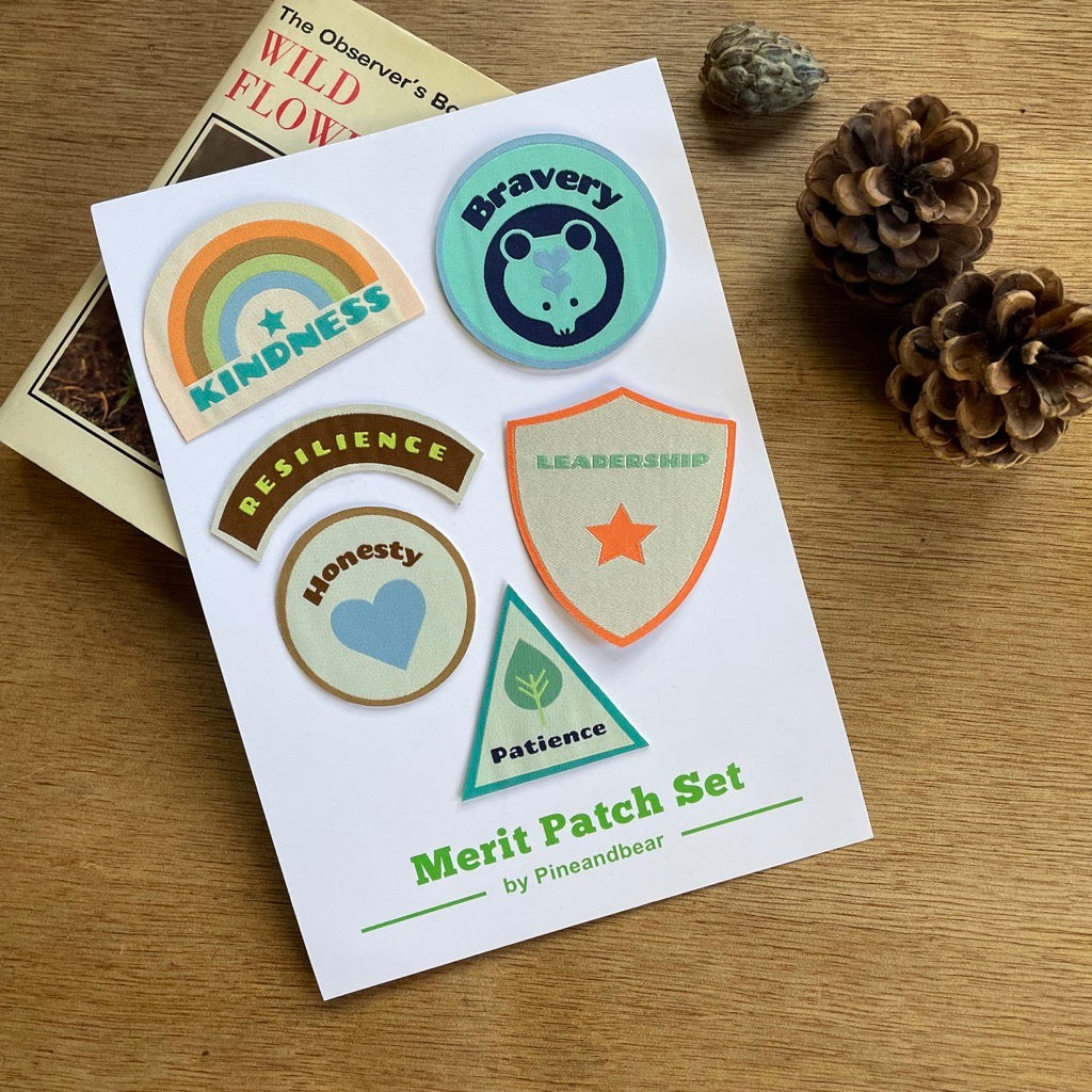 Merit Patches For Children on a white presentation card with pine cones and a book.
