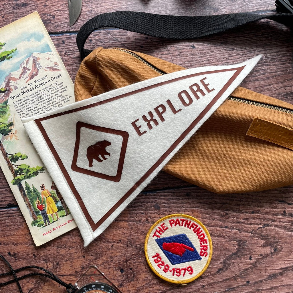 Explore mini pennant flag in brown laying on a brown bag with a vintage patch and map