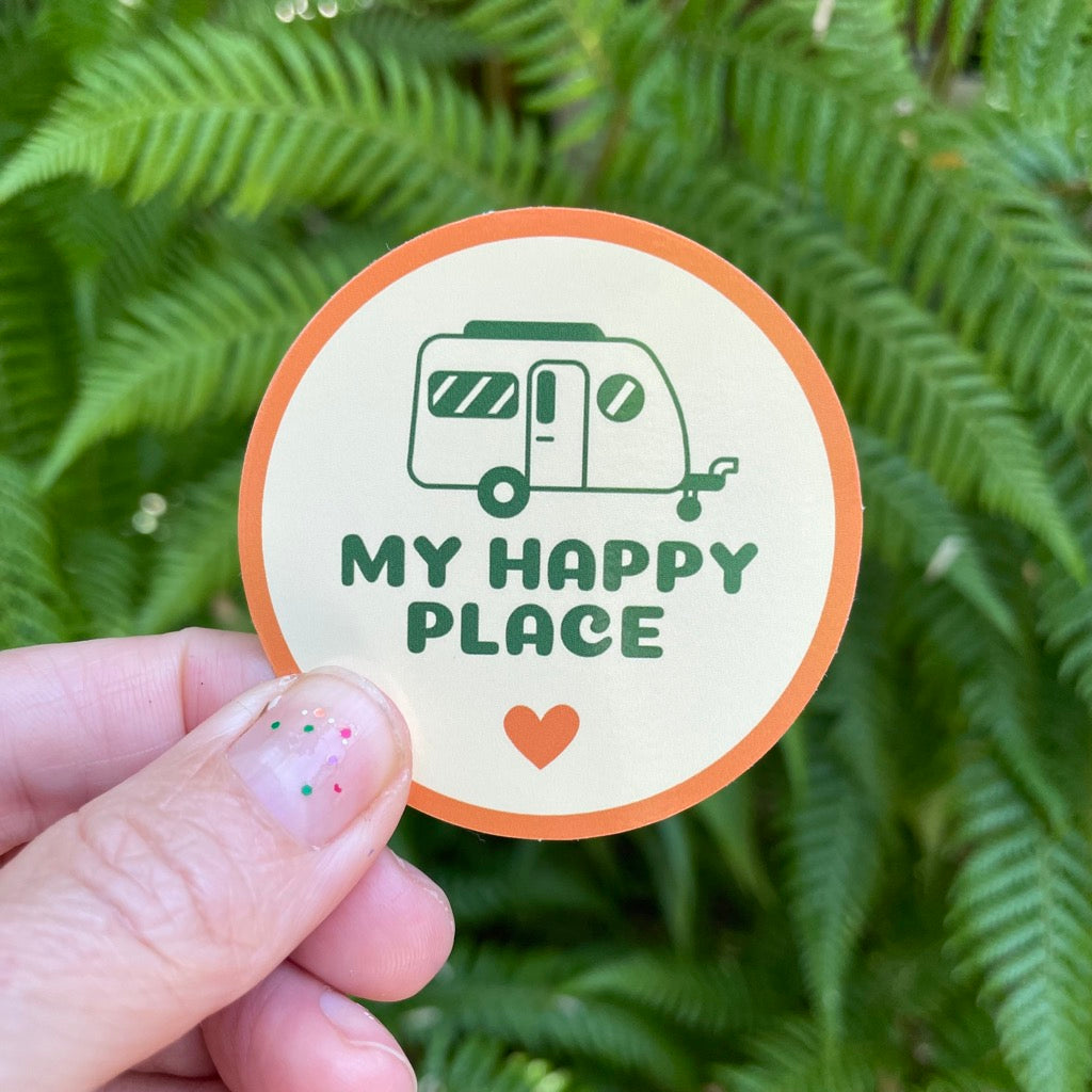 My Happy place vinyl camping sticker being held in front of some ferns.