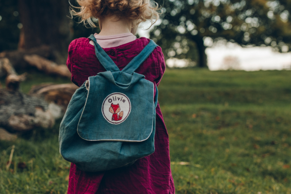 A young girl standing with a rucksack on and an embroidered name patch with a fox design