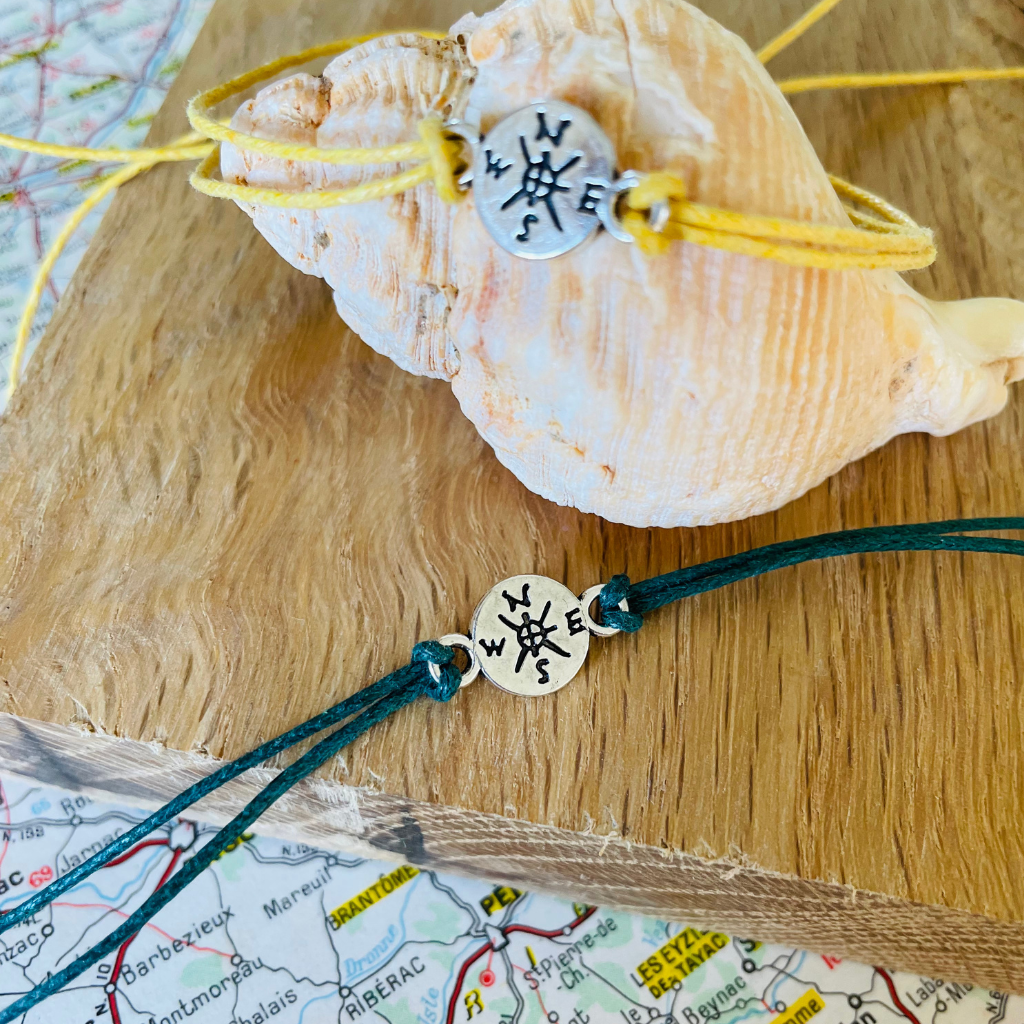 Compass adventure wish bracelets displayed on a shell and a piece of wood.