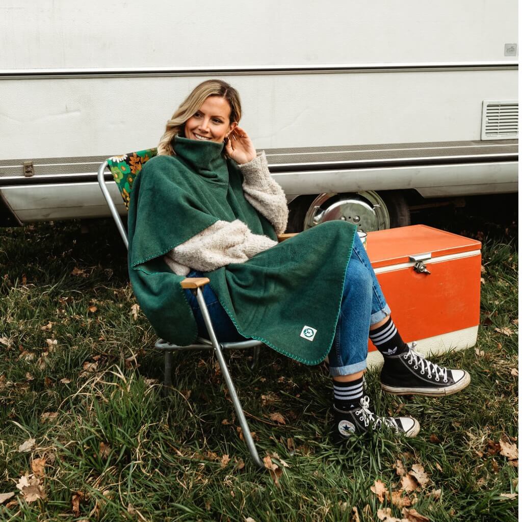 a lasy wearing a green camp blanket poncho, sitting in a deck chair