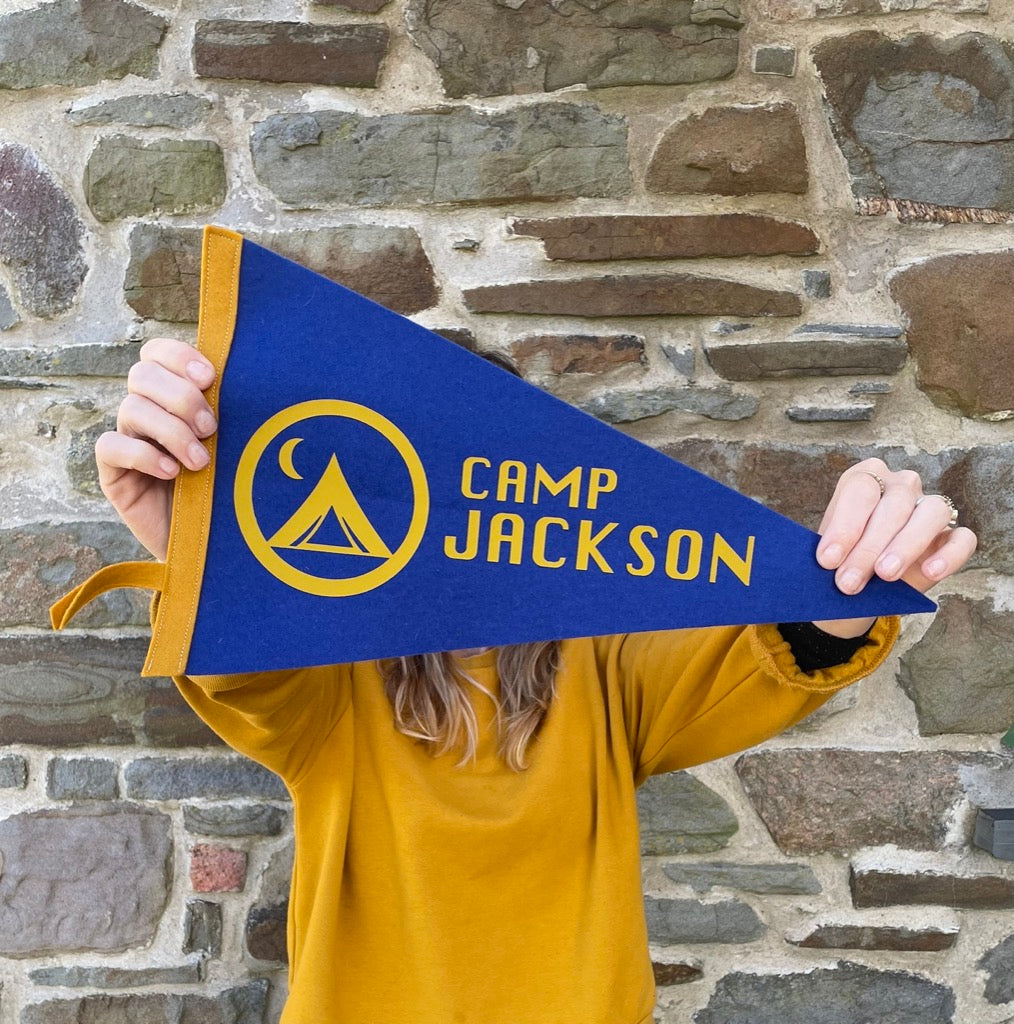 Custom Camp Flag in blue and mustard being held by a girl in front of a stone wall.