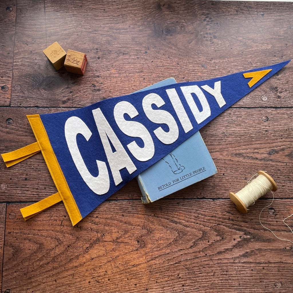 Personalised pennant flag in blue, white and mustard on a wooden table and peter pan book