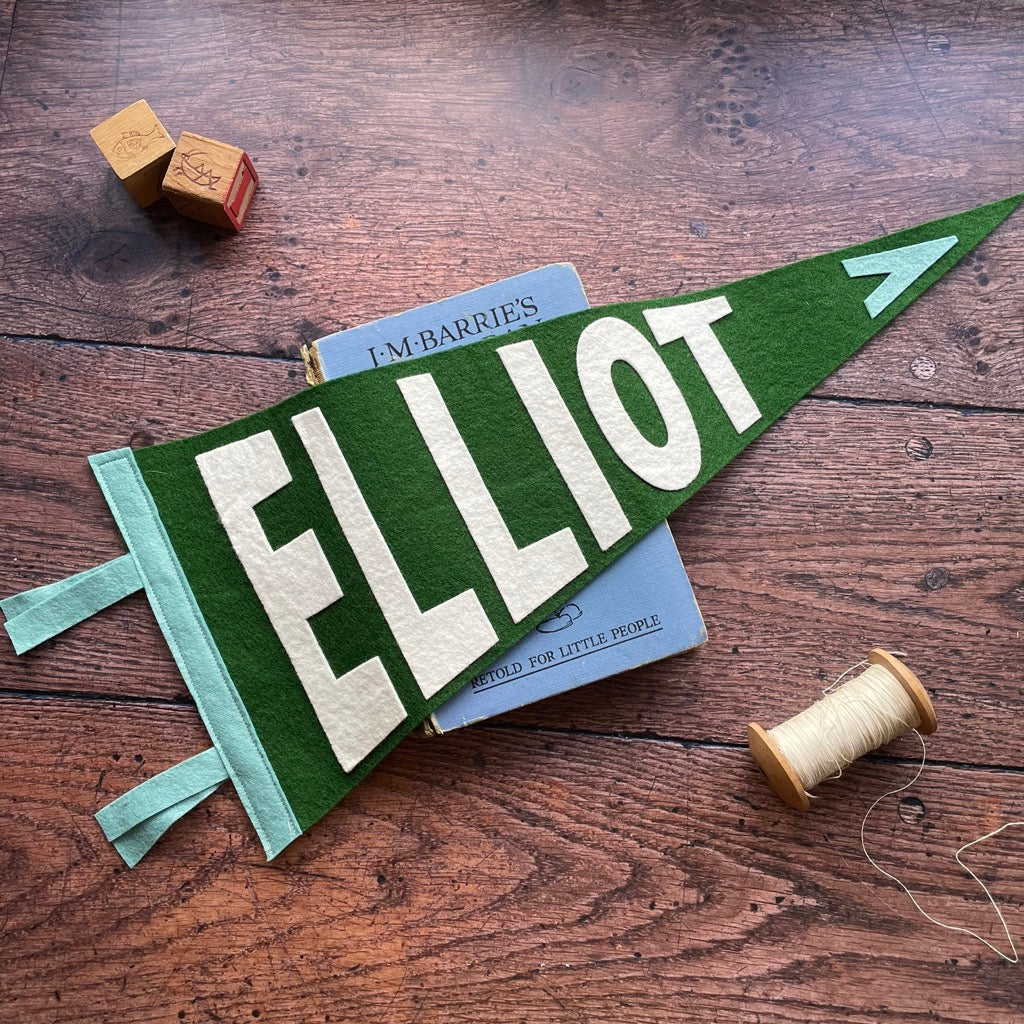Personalised pennant flag in green, white and tuquoise on a wooden table and peter pan book