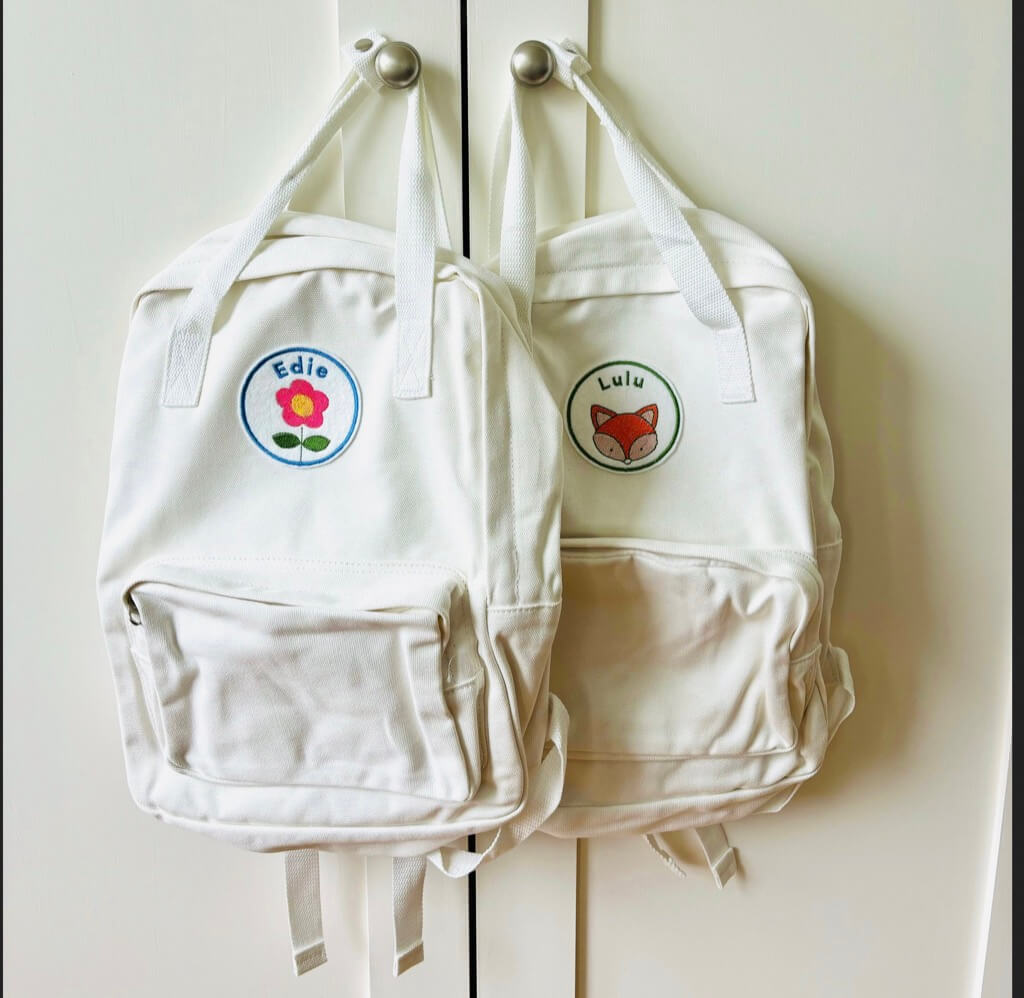 Two cream rucksacks decorated with felt embroidered name patches