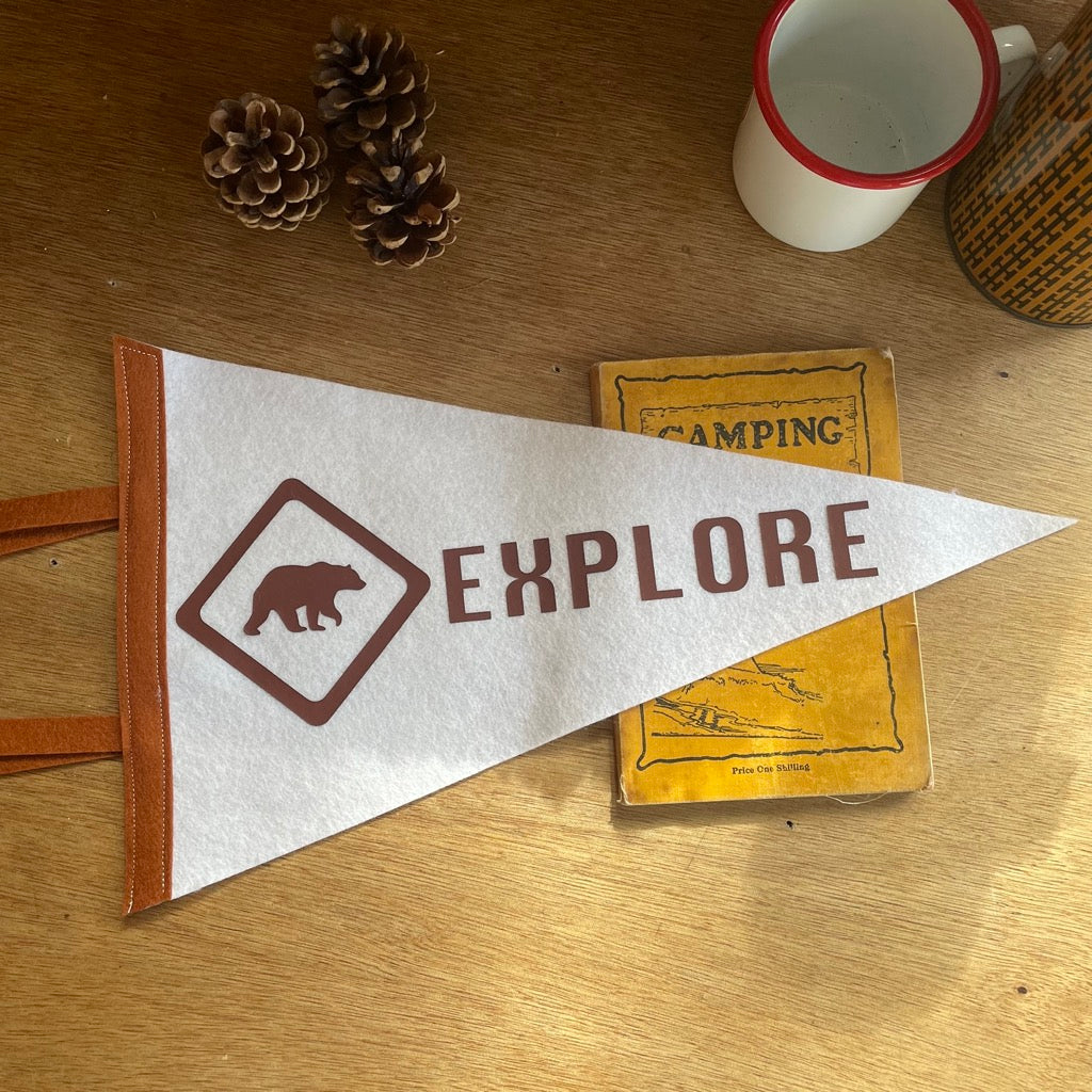 Explore pennant flag in white and bown with a bear design on a wooden desk.