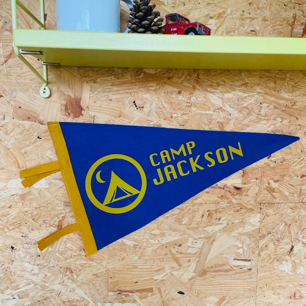Custom Camp Flag in blue and mustard on a wall with shelves above 