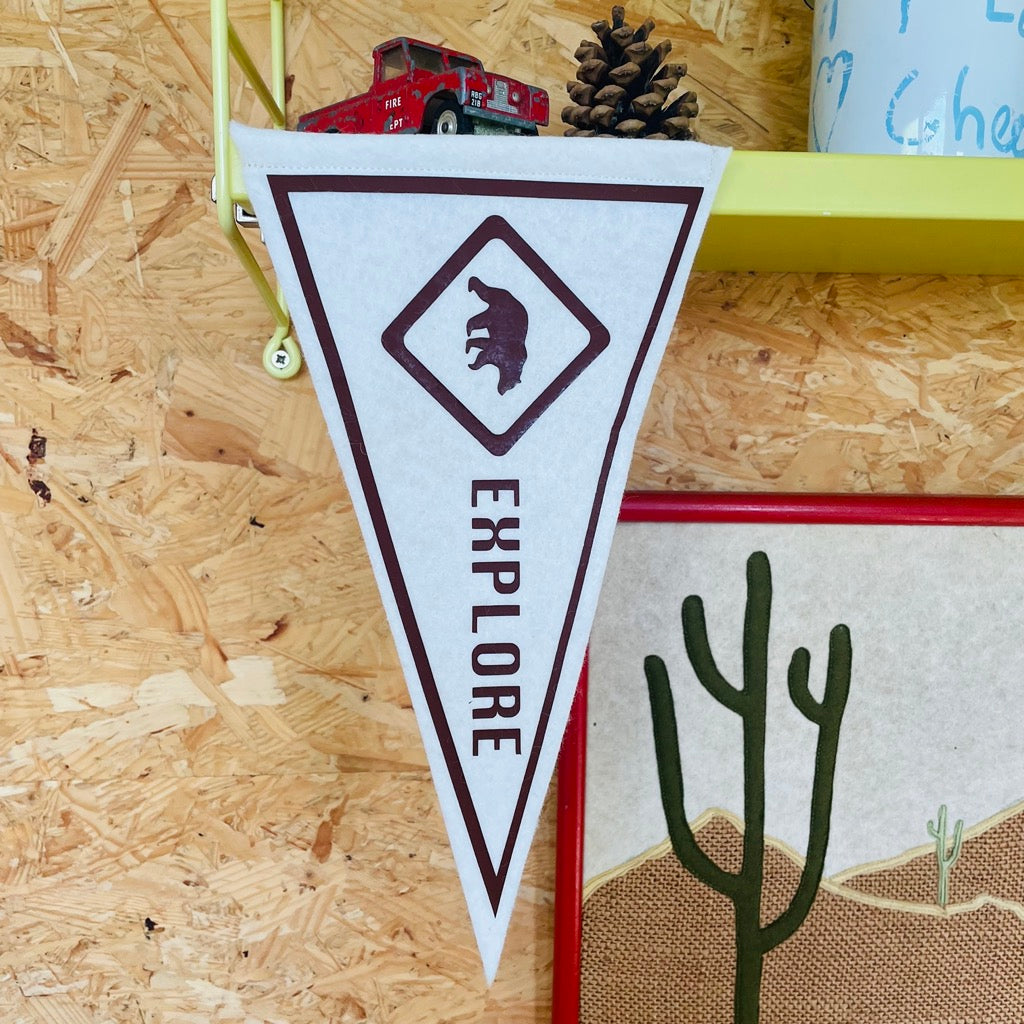 explore mini pennant flag in brown and white with a bear design on a yellow shelf