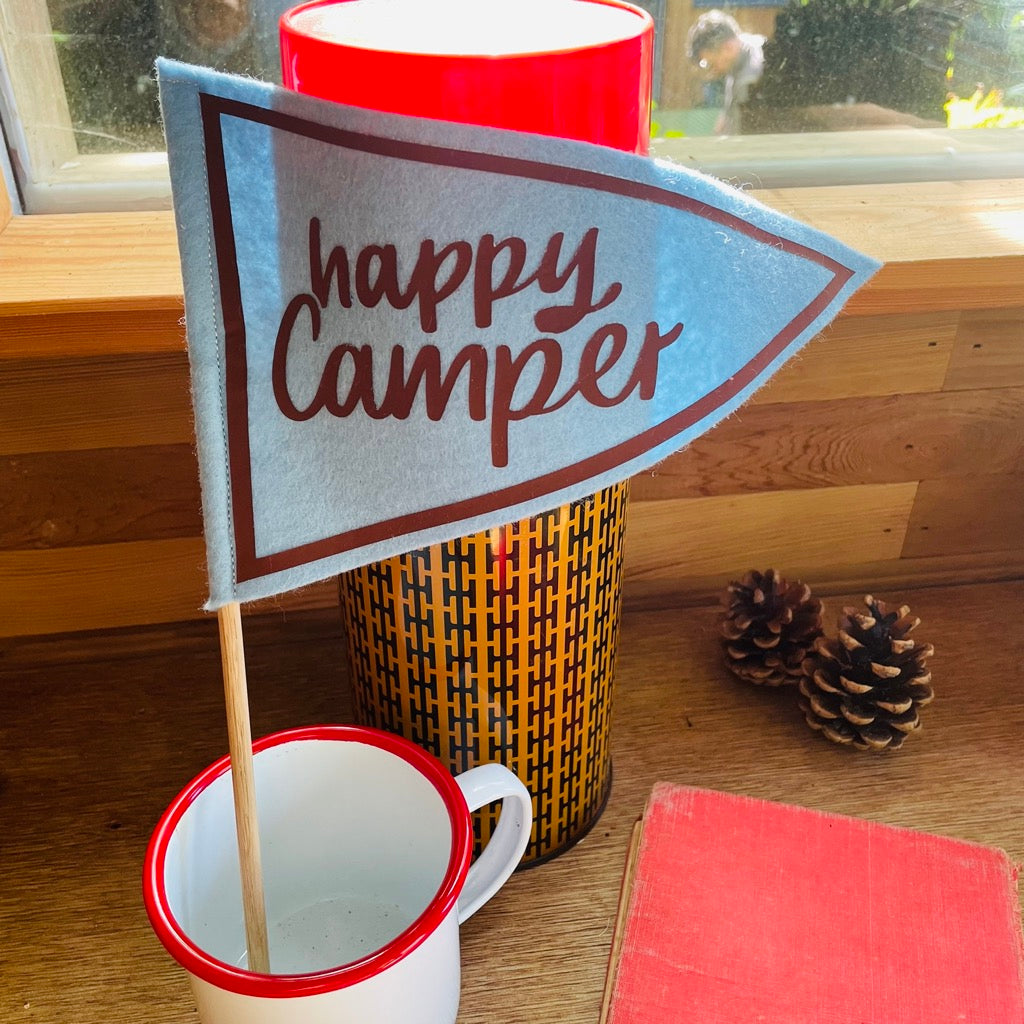 Happy camper flag on a pole in blue and brown in a enamel mug and camping flask