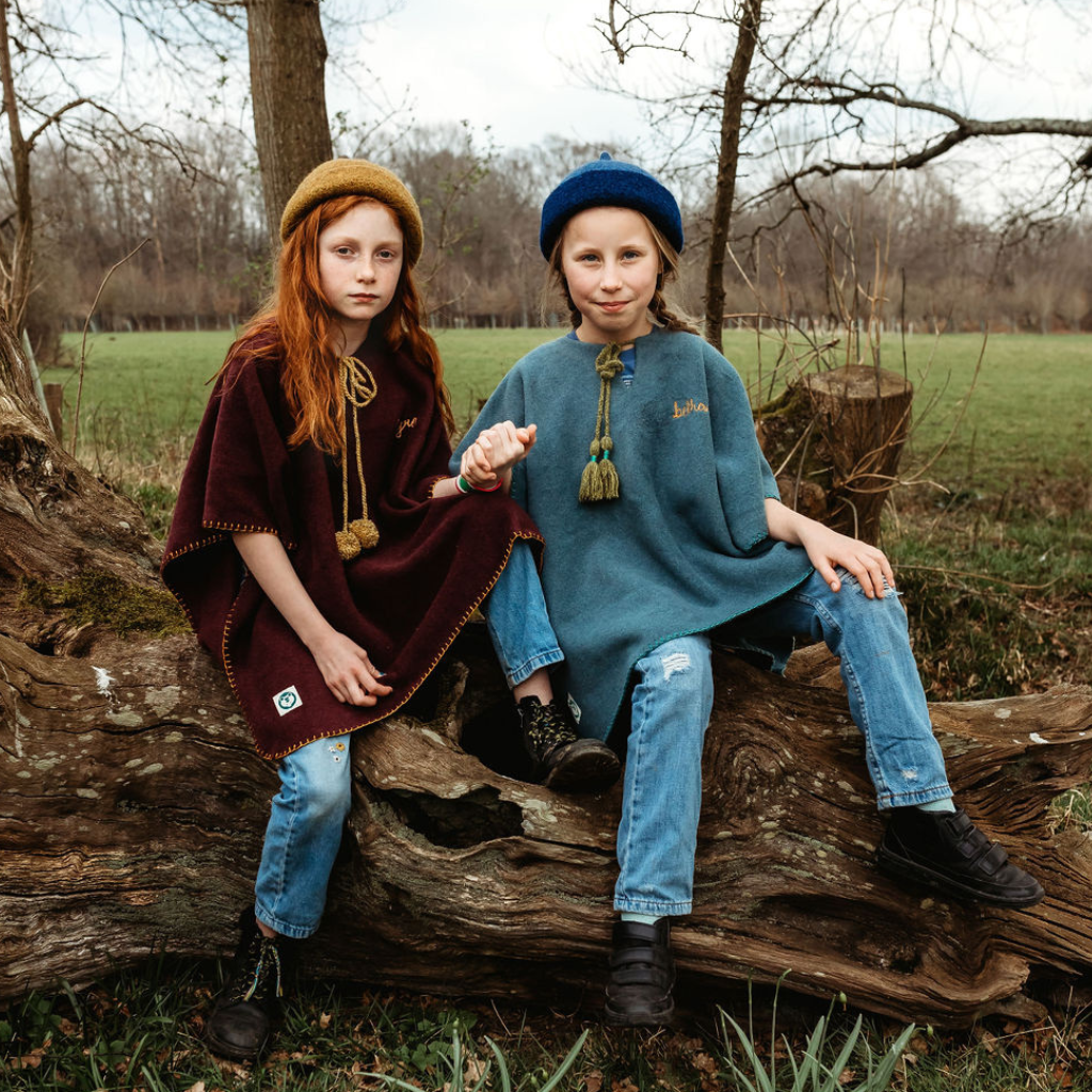 two girls sitting on a log outdoors wearing camp blanket ponchos