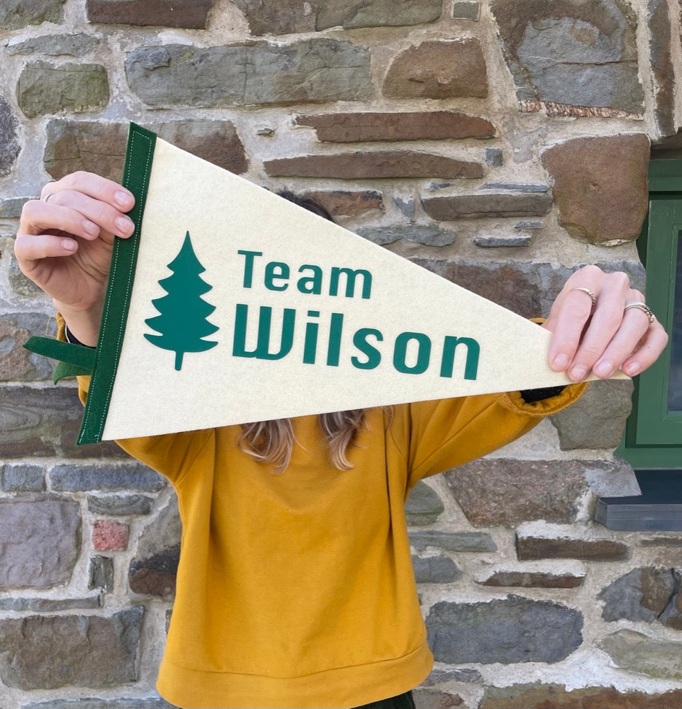 Team pennant flag in cream and green with a tree design being held up in front of a stone wall