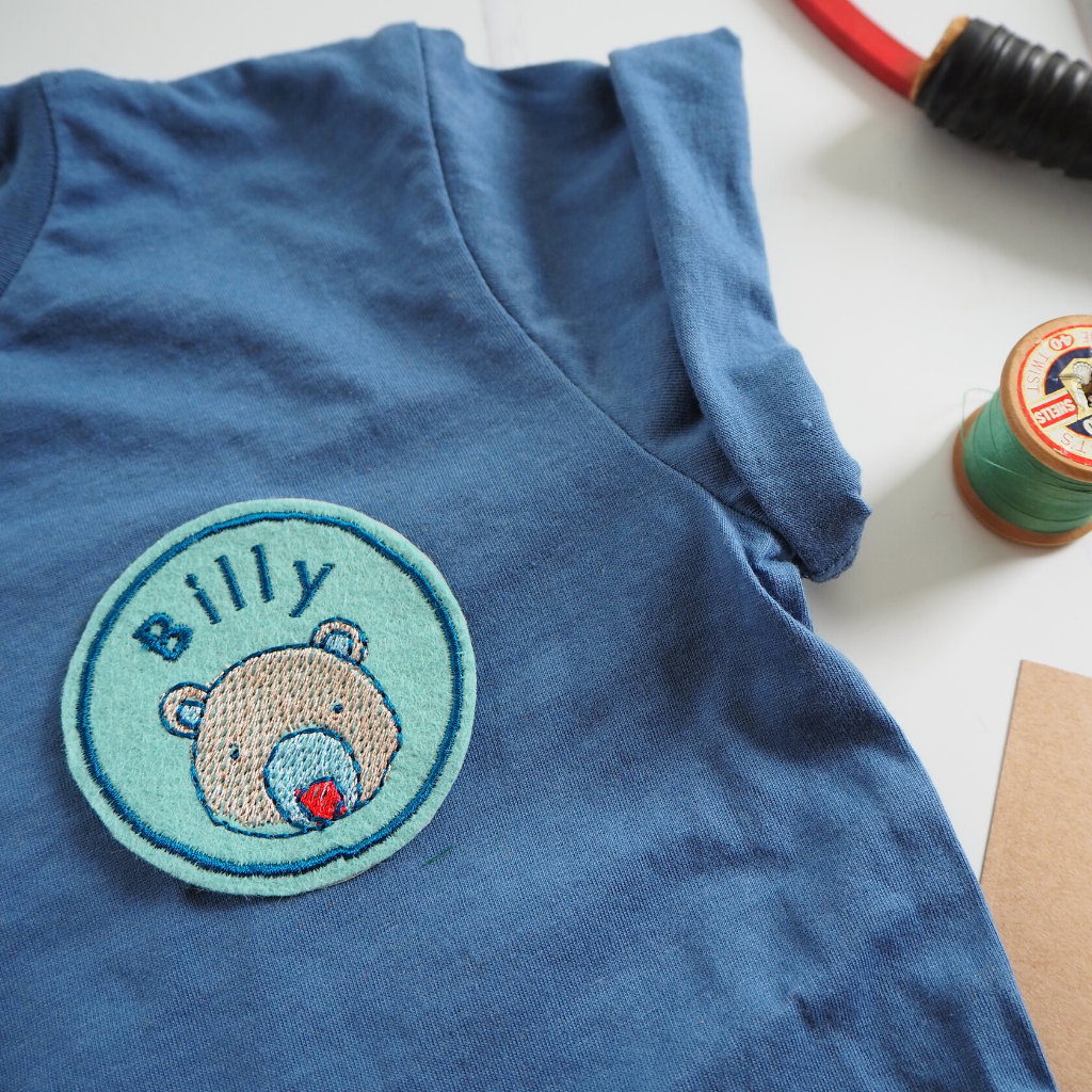A personalised embroidered name patch with a cute bear design, shown on a T-shirt.
