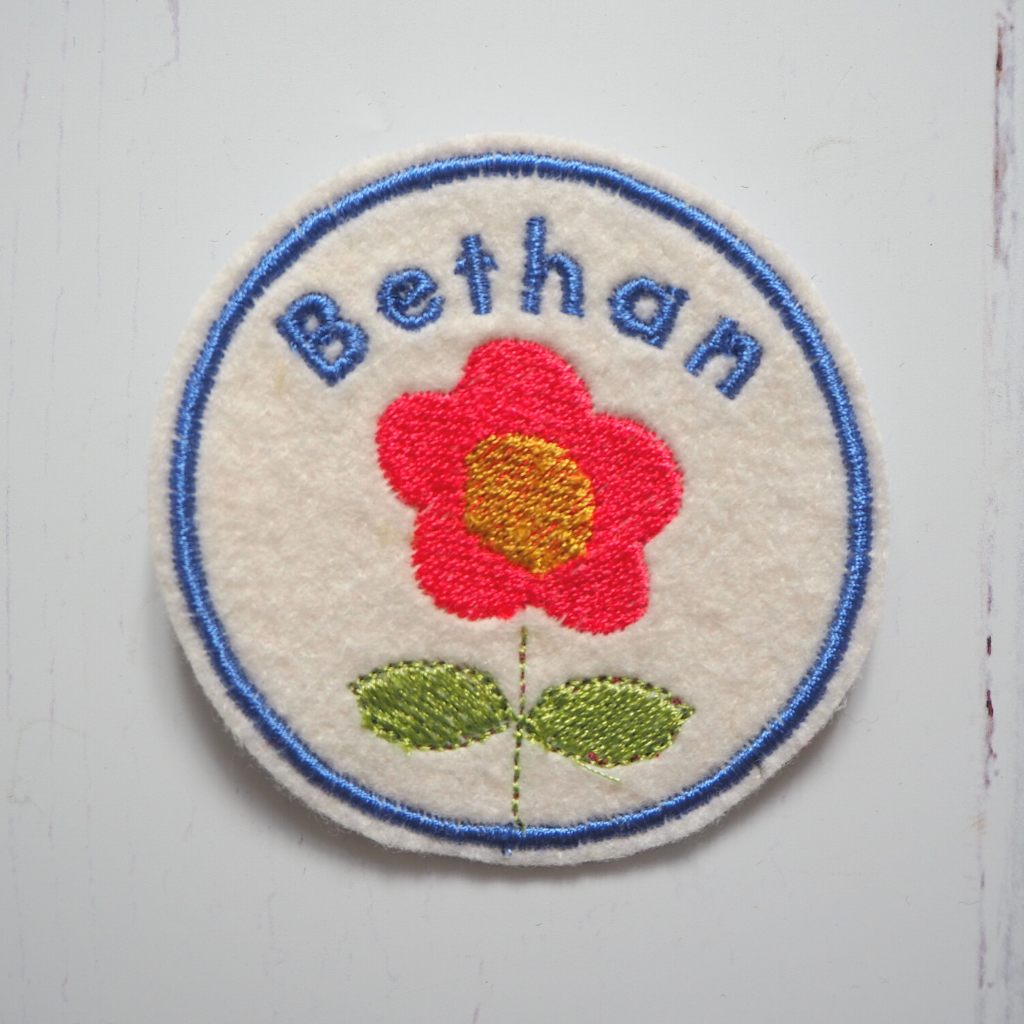 An embroidered name patch with a flower design.